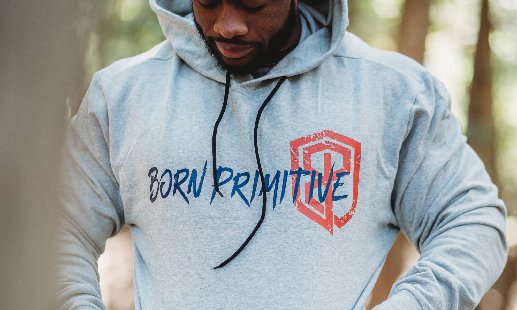 Man wearing a light grey heather hoodie with a navy and red typographic logo printed along the chest.